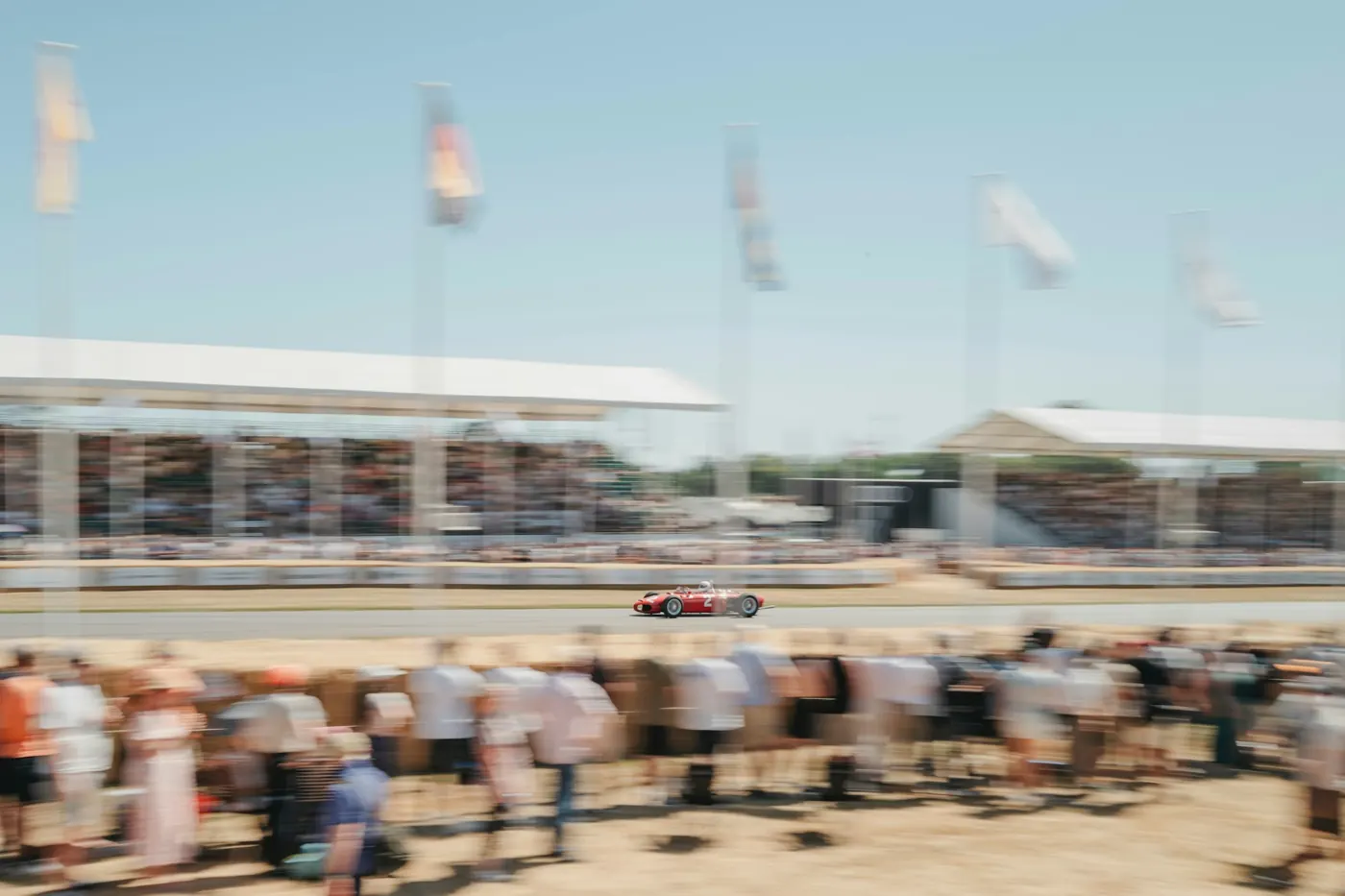 A red racing car passing a packed grandstand