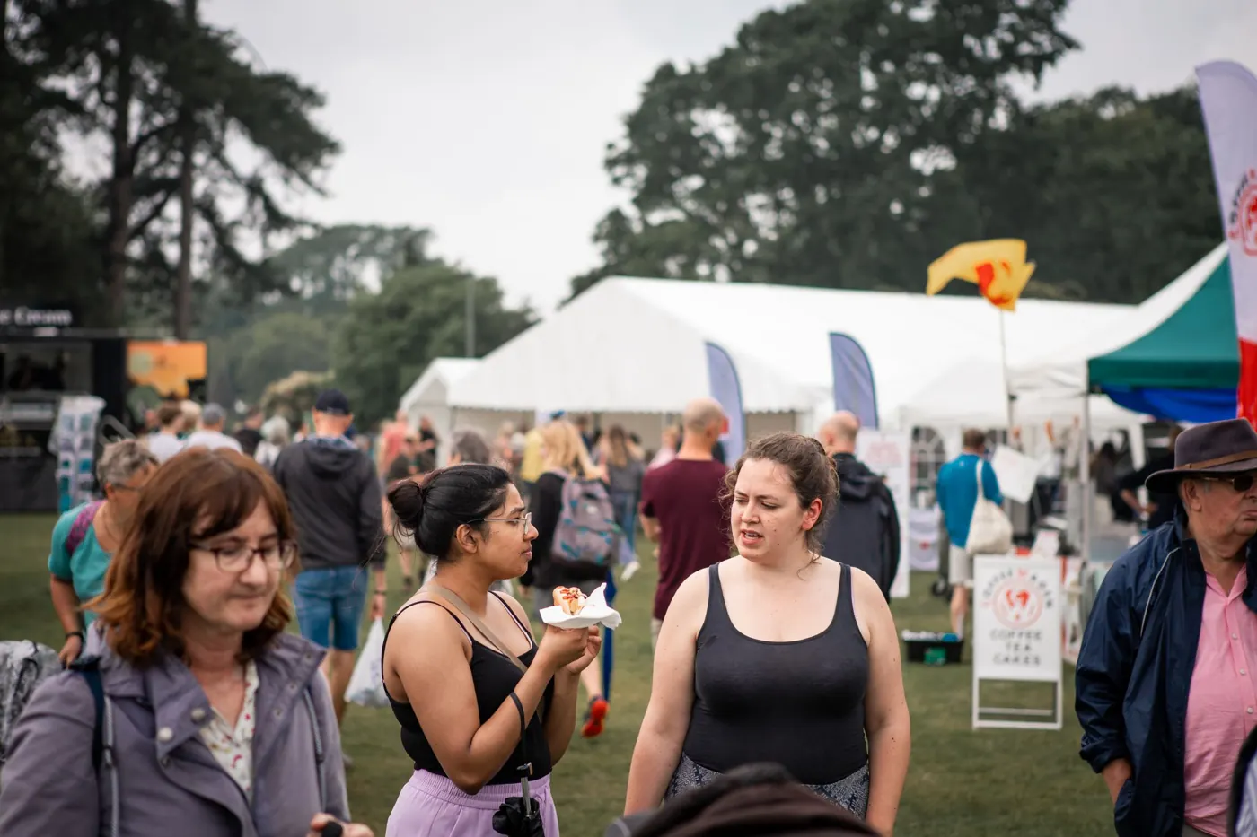 Guests with food in front of stalls and a marquee at an outdoor event
