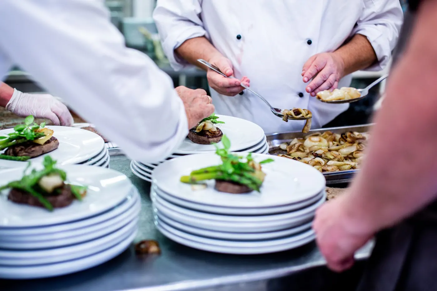 Chefs plating beef and asparagus onto a row of white plates