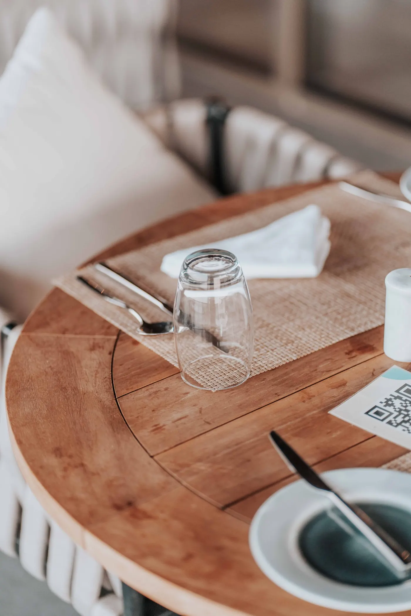 A QR card on a wooden restaurant table beside an upturned glass and cutlery